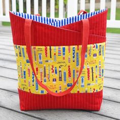 a red and yellow tote bag sitting on top of a wooden table next to a white fence