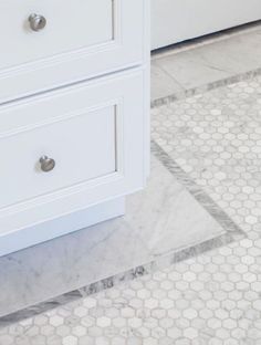 a white bathroom with hexagonal tile flooring and drawers on either side of the bathtub