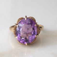 A Vintage 9 carat gold Amethyst ring. This beautiful piece displays a gorgeous purple stone in the clutches of a pretty gold setting. CONDITION: Wear consistent with age and use. Please see photos for more detail. ASSAYED IN LONDON CIRCA.1977 STONE FACE SIZE: 10mm x 12mm BAND WIDTH: 2mm SETTING HEIGHT: 7mm RING SIZE: UK: M 1/2 | US: 6 1/4 WEIGHT: 3.8 grams (UUZ) Vintage Amethyst Ring Gold, Formal Amethyst Ring In 14k Gold, Formal 14k Gold Amethyst Gemstone Ring, Purple Amethyst Ring With Prong Setting In 14k Gold, Heirloom Solitaire Purple Amethyst Ring, Gold Solitaire Amethyst Ring For Formal Occasions, Purple Amethyst Ring In 14k Gold, Formal Purple Amethyst Ring In 14k Gold, Formal 14k Gold Purple Amethyst Ring