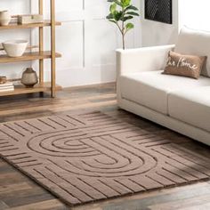 a living room with a white couch and brown rug on top of the wooden floor