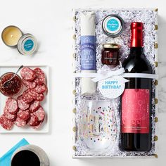 an assortment of food and drinks in a gift box on a white table with condiments