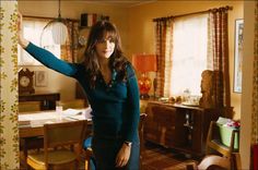 a woman standing in a living room next to a dining room table with chairs and a clock on the wall