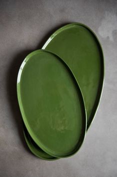 two green plates sitting next to each other on top of a gray tablecloth covered floor