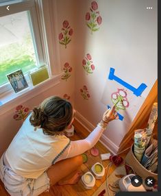 a woman is painting flowers on the wall with blue tape and watercolors in front of her