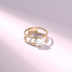 a gold ring with a white diamond in the center on a light pink background,