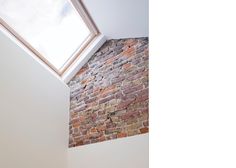 a bathroom with a skylight above the toilet and bathtub in front of a brick wall