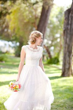 a woman in a white dress is walking through the grass with her bouquet on her hand