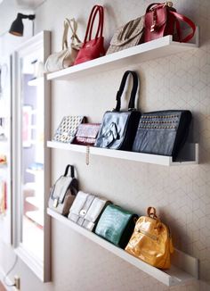 several purses are hanging on the wall in a room with white shelving and shelves