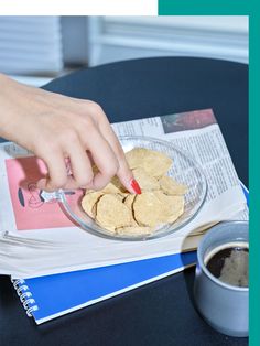 a person is picking up some food from a bowl on a table next to a cup of coffee