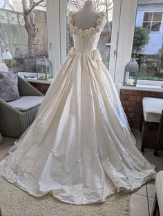 a white wedding dress on display in front of a window with a couch and chair