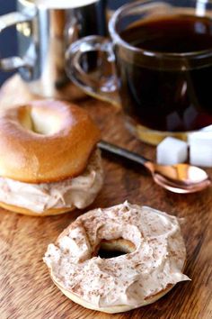 two donuts sitting on top of a wooden table next to a cup of coffee