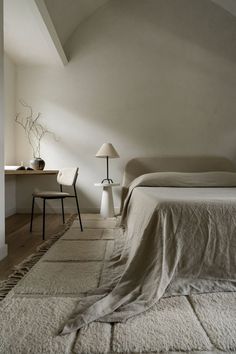 a bed sitting in a bedroom next to a lamp on a table and two chairs