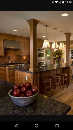 a bowl of apples sits in the middle of a kitchen with an island and bar stools