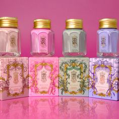 four jars with different designs on them sitting next to each other in front of a pink background