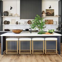 three stools sit in front of an island with plants and bowls on the counter