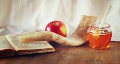 an apple, pipe, book and honey on a wooden table with a white curtain