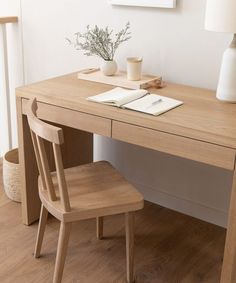 a wooden desk with two chairs and a lamp on it in a white walled room