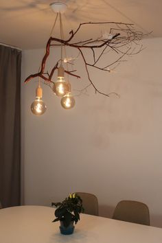 a white table topped with a vase filled with flowers next to a light bulb chandelier