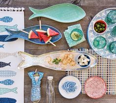 an assortment of plates and bowls on a wooden table with fish, watermelon, lemons