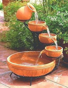 an outdoor fountain with water pouring out of it's sides and potted plants in the background