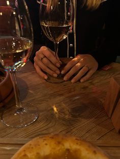 a woman sitting at a table with two wine glasses in front of her and a pizza on the side