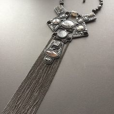 a silver necklace with many beads and chains hanging from it's center, on a gray surface