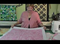 a woman standing in front of a sewing machine holding up a piece of pink fabric