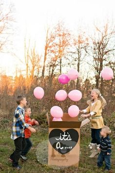 two children and an adult playing with balloons in a cardboard box on the grass outside