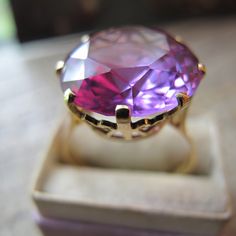 18k Yellow Gold Basket Set with a Color Changing Purple to Pink Synthetic Statement Gemstone-Look Stone Cocktail Ring. True Vintage, Fully Hallmarked Assay Marked, Foreign Made Fine Gold, looks to be Egyptian marks. Tested for 18k gold. True vintage age, Estate Fine Gold Unique Jewelry. Looks mostly like an amethyst, again color changing and manmade aka synthetic gem look stone.  16 MM round stones (11 to 15 carats, without removing it from the setting the exact carat weight is unknown, this is an      approximation)  2.4 MM Band Width  Resembles the color changing ability of an Alexandrite  Fully hallmarked for 18k gold, tested professionally too  9 1/4 Size  Cocktail Statement  6.6 grams  1950 to 1970 time window, I believe there is a mark for the year.  Stone color varies in different l Elegant Faceted Gemstones For Formal Occasions, Heirloom Amethyst Ring In Yellow Gold, Heirloom Yellow Gold Amethyst Ring With Round Cut, Heirloom Yellow Gold Amethyst Ring, Luxury Purple Jewelry For Collectors, Luxury Faceted Gemstones For Anniversary, Yellow Gold Amethyst Ring For Wedding, Luxury High Luster Gemstones For Formal Occasions, Heirloom Yellow Gold Round Amethyst Ring