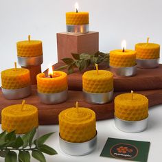 many yellow candles are placed on a wooden tray next to some green leaves and a card