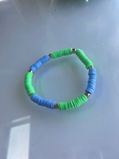 a blue and green beaded bracelet sitting on top of a white table next to a vase