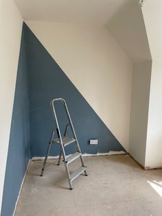 an empty room with a ladder in the corner and a blue painted wall behind it