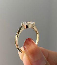 a hand holding a gold ring with a diamond in it