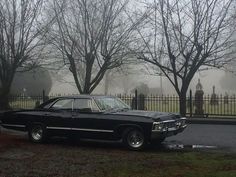 an old black car parked in front of a cemetery