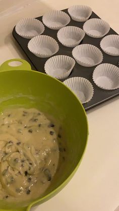 a green bowl filled with batter next to muffin tins on a white counter