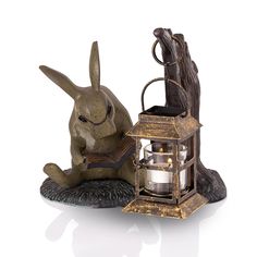 a statue of a rabbit reading a book next to an old fashioned lantern and candle holder