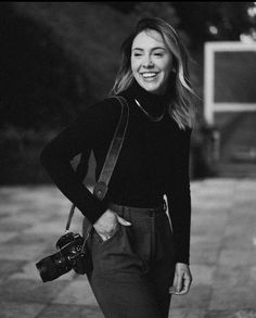 a black and white photo of a woman holding a camera smiling at the camera man