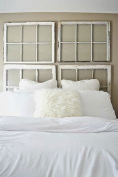 a white bed topped with pillows next to a wall mounted headboard in a bedroom