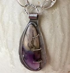 I bought this gorgeous piece of Amethyst Sage Agate a few years ago, and finally came up with a design to highlight it. The stone has gorgeous shades of purple and tan with dark variegated lines.  I tried pairing it with several combinations of stones before landing on these beautiful, faceted  Ametrine beads on one side of the design.  All of the silver chain and other findings are Sterling Silver.  I added a large clasp near the front of the necklace and included it as part of the asymmetrical Artisan Sterling Silver Purple Jewelry, Purple Artisan Sterling Silver Jewelry, Artisan Purple Sterling Silver Jewelry, Artisan Sterling Silver Jewelry In Purple, Artisan Purple Gemstone Jewelry, Artisan Purple Amethyst Jewelry, Teardrop Amethyst Jewelry With Natural Stones, Oval Amethyst Necklace With Natural Stones, Unique Purple Teardrop Jewelry