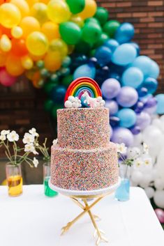 a multi - layer cake with sprinkles and a rainbow decoration on top