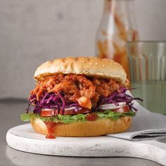 a pulled pork sandwich with cole slaw on a cutting board next to a glass of water