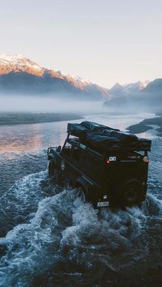 a black truck driving through water with mountains in the backgrouds behind it