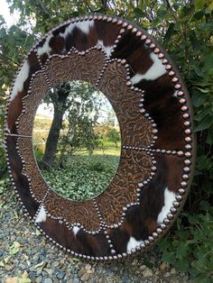 a cowhide mirror sitting on top of a gravel ground next to a tree and bushes