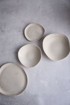 three white plates sitting next to each other on a gray tableclothed surface, with one empty plate in the middle