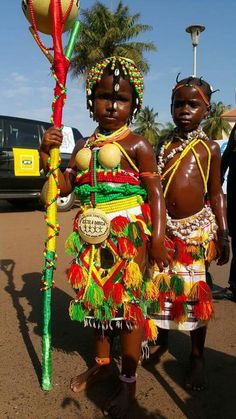 two young children dressed in colorful costumes holding a stick and ball on the street with palm trees in the background