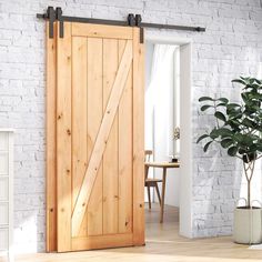 a white brick wall with a wooden sliding door and potted plant next to it