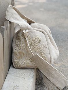 a white purse sitting on the side of a wooden bench next to a cement wall