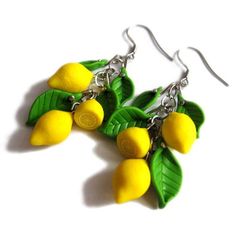 two lemons and green leaves are hanging from the earwires of these earrings