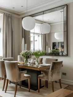 the dining room table is surrounded by beige chairs and white vases with greenery