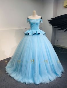 a light blue ball gown on display in a room with black angel wings behind it